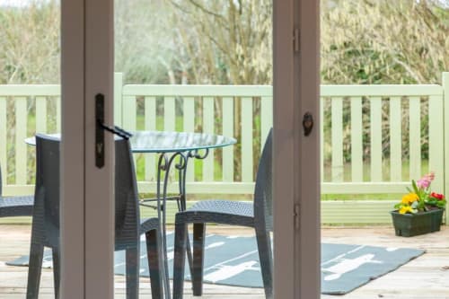 Covered patio with glass table, dark chairs, and garden view at Les logis de Kergoulou cottage in Concarneau