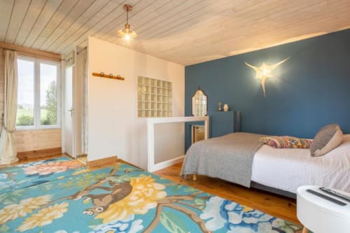 Bright cottage bedroom at Les logis de Kergoulou in Concarneau with blue accent wall, garden view, and colorful rug