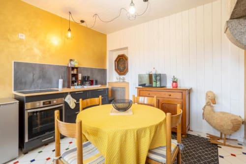 Bright yellow kitchen-dining room with round table, wooden chairs, and black stovetop at Gîte Le Studio Terrasse, Concarneau