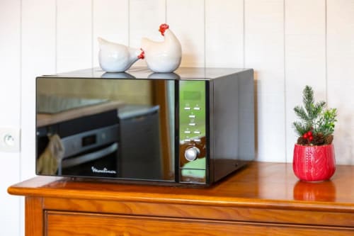 Microwave oven on wooden table with white ceramic chickens and potted succulent plant at Les logis de Kergoulou cottage in