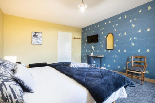 Bedroom with yellow and blue walls, double bed with navy bedding, flat-screen TV, and wooden chair at Les logis de Kergoulou,