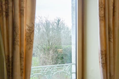 Ornate curtains frame a view of bare winter trees and garden at Les logis de Kergoulau, Concarneau B&B