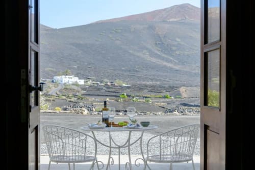 Open doors to terrace with table setup overlooking volcanic mountain landscape at Finca de La Geria cottage in Lanzarote