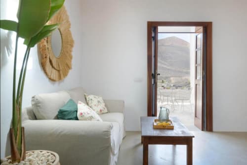 Bright living room at Finca de La Geria cottage with cream sofa, mountain views through open doors, and potted plant decor in