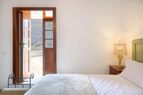 Bright bedroom at Finca de La Geria cottage with bed, wooden door opening to mountain views, and bedside lamp in Yaiza