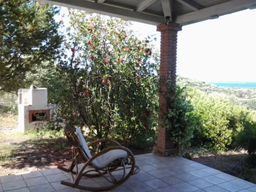 Shaded veranda with rocking chair overlooking sea view at Orosei villa in Sardinia