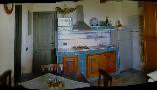Cottage kitchen and dining area in Orosei villa with blue tile backsplash, wooden cabinets, and dining table