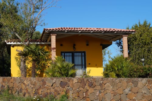 Bright yellow villa cottage in Orosei with stone wall, terracotta roof, sea view, surrounded by Mediterranean vegetation and