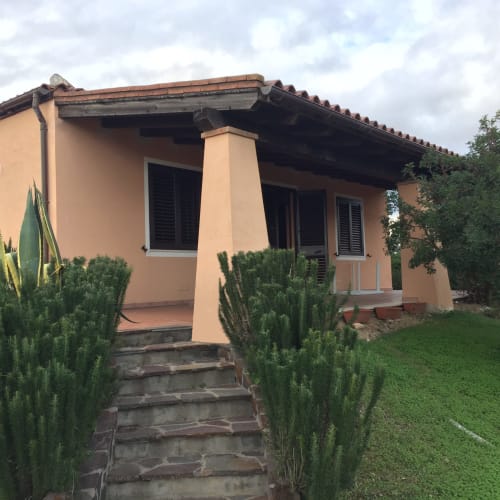 Peach-colored villa in Orosei with terracotta roof, front porch, green landscaping, and sea view access