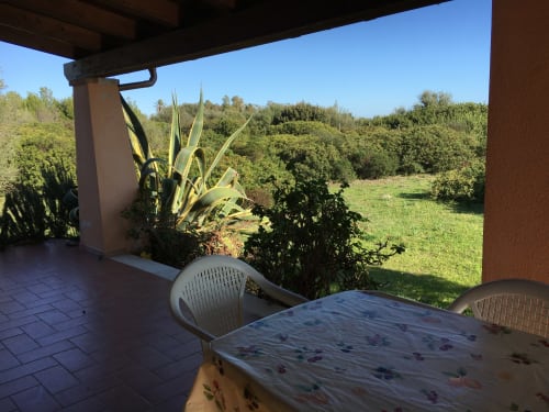 Shaded veranda with dining table overlooking lush gardens at Domo Giulia villa in Orosei, Italy