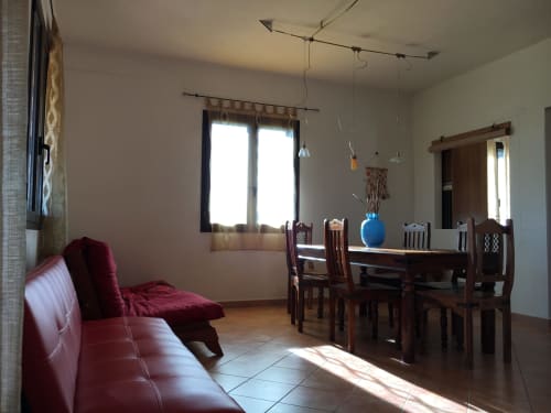 Bright open-plan living room with burgundy sofa, dining table, and sea view at Domo Giulia villa in Orosei