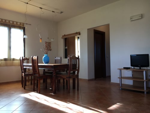 Bright dining room with wooden table and chairs, TV stand, open-plan living area in Orosei villa with sea views