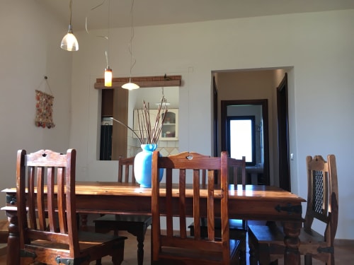 Dining room with wooden table and chairs, pendant lights, and blue vase with branches in villa in Orosei