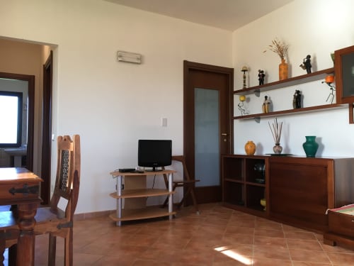 Modern living room in Orosei villa with wooden shelving, TV stand, and terracotta flooring