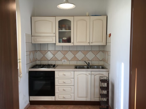 Compact kitchen with cream cabinets, gas cooktop, black oven, and decorative tile backsplash in Orosei villa