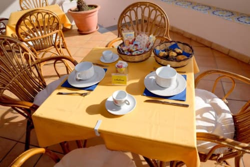 Terrazza colazione soleggiata dell'Hotel Principe di Rinella con tavolo giallo, sedie in vimini, mise en place e snack