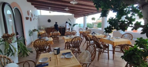 Terrazza con tavoli e sedie in rattan dell'Hotel Principe di Rinella, arredata con piante verdi a Rinella, Italia