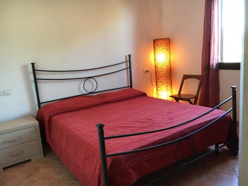 Bedroom with red bedspread, black metal bed frame, and decorative floor lamp in villa Domo Giulia at Orosei accommodation