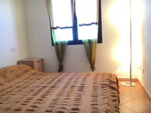 Bedroom with patterned bedspread, window with sea view, TV, wooden nightstand, and tile flooring in Orosei villa
