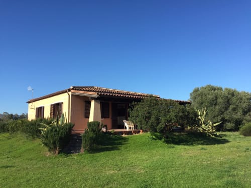 Villa Domo Giulia a Orosei con tetto in coppi, muri gialli e portico arredato con vista sul prato verde