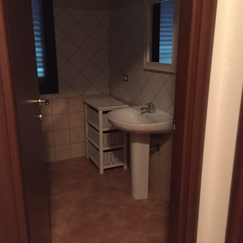 Modern bathroom with pedestal sink, white storage unit, and tiled walls in Domo Giulia villa, Orosei