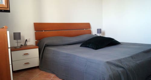 Modern bedroom in Orosei villa with orange headboard, gray bedding, black pillow, and wood nightstand with lamp