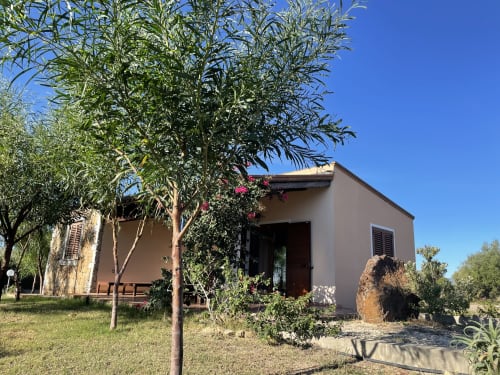 Rustic villa in Orosei with beige walls, lush green vegetation, flowering bougainvillea, and shaded porch in Mediterranean