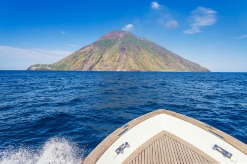 Vista dalla prua della barca verso l'isola di Stromboli con mare blu e cono vulcanico presso l'Hotel Principe di Rinella, Sicilia