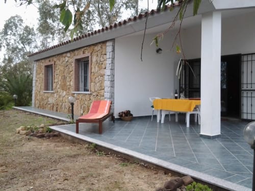 Stone villa veranda in Orosei with furnished patio, white columns, and sea view garden setting