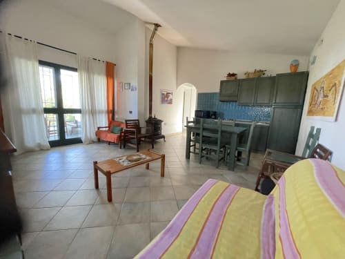 Open-plan villa living area with kitchen, dining table, stove, and sea-view doors in Orosei, Italy