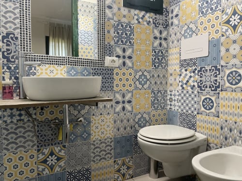Modern bathroom with patterned blue, yellow and gray tiles, vessel sink, toilet and bidet in Orosei villa