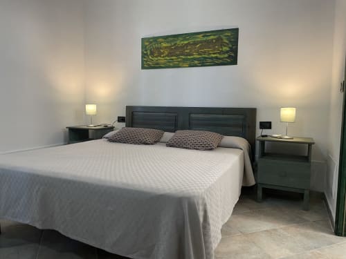 Modern villa bedroom in Orosei with dark green bed, white linens, patterned pillows, bedside lamps, and abstract art above