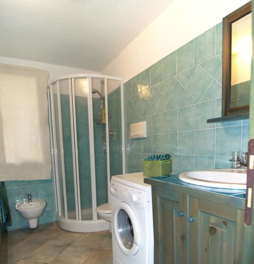 Modern bathroom with shower, sink, washing machine, and turquoise tile in Orosei villa