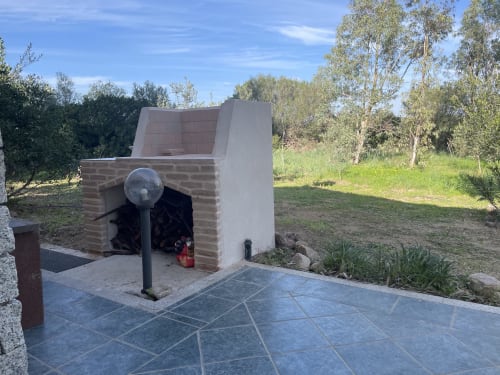Wood-fired pizza oven at Loddo Paola villa in Orosei with patio, red fire extinguisher, and eucalyptus trees