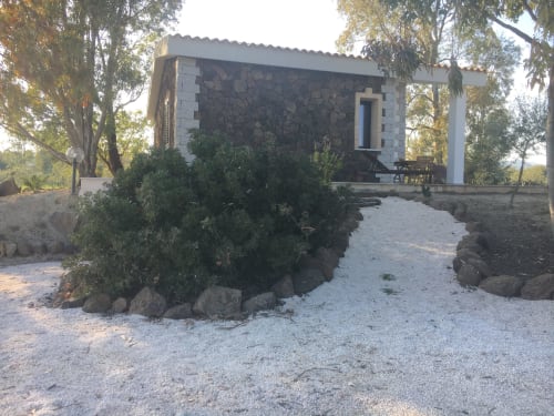 Rural stone villa in Orosei with garden pathway, surrounded by Mediterranean trees and landscaping