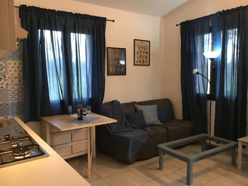 Modern villa living space in Orosei with dark sofa, wood table, black curtains, and open kitchen area
