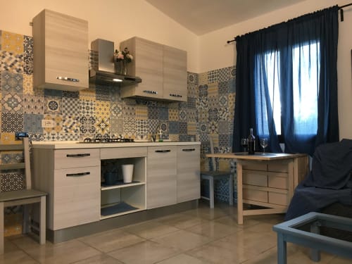 Modern kitchen with patterned tile backsplash, light wood cabinets, and open living area in Orosei villa
