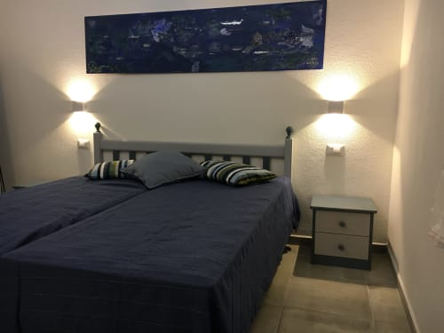 Modern bedroom at Sa Tanca De su Catreathu villa in Orosei with dark bedding, striped pillows, wall sconces, and artwork