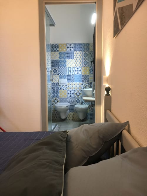 Bedroom view into ensuite bathroom with decorative blue and yellow tiles in Orosei villa rental