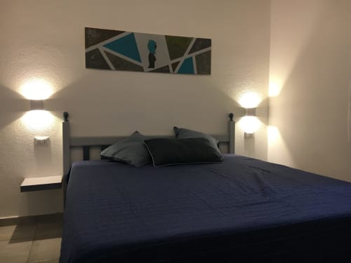 Modern bedroom with dark blue bedding, pillows, and wall sconces in Sa Tanca villa, Orosei