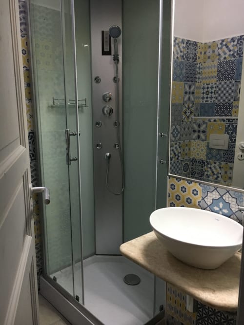 Modern bathroom with walk-in shower, white vessel sink, and patterned blue-yellow tile backsplash at Sa Tanca De su Catreathu