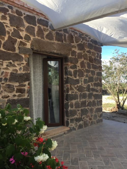 Ingresso di villa in pietra con porta in legno e patio coperto a Sa Domo De Mannoi a Orosei, Italia, decorato con piante fiorite