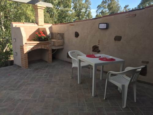Terrazza esterna di Villa Sa Domo De Mannoi a Orosei con forno a legna in mattoni, tavolo da pranzo e pavimentazione in pietra