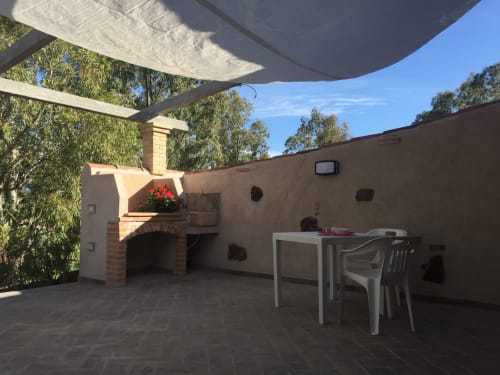 Veranda della villa di Orosei con forno a legna per pizza, tavolo da pranzo e pergolato ombreggiato con vista sugli alberi