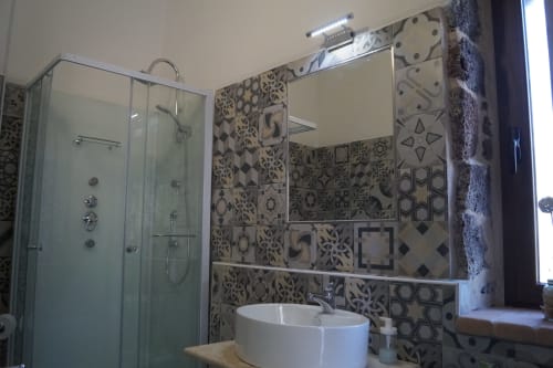 Bagno moderno con parete piastrellata decorativa, lavabo rotondo bianco e doccia in vetro alla villa Sa Domo De Mannoi a Orosei