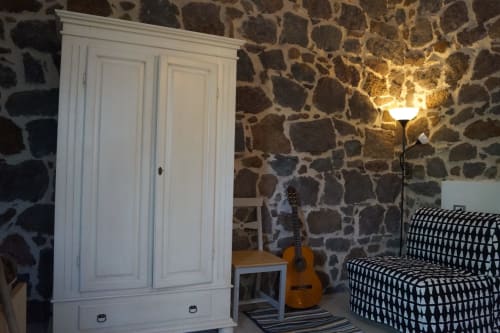 Camera da letto in villa in pietra a Orosei con guardaroba bianco, chitarra acustica, poltrona decorata e illuminazione calda