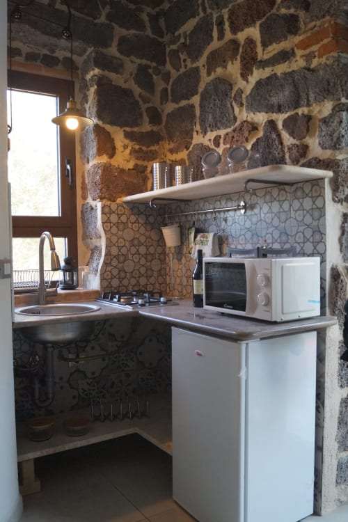 Cucina compatta nella villa di Orosei con muri in pietra, microonde bianco, piano cottura, lavello e piastrelle decorate