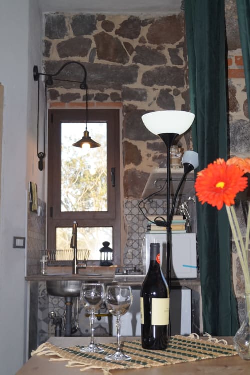 Interno in pietra rustica nella villa Sa Domo De Mannoi a Orosei con bottiglia di vino, fiore rosso e eleganti lampade nere