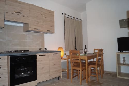 Modern villa kitchen and dining area in Orosei with wooden cabinets, dining table, TV, and beige curtains