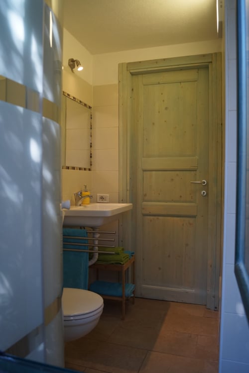 Bright bathroom with white tiles, wooden door, sink, toilet, and blue towel rack in Sa Tanca De Mannoi villa, Orosei